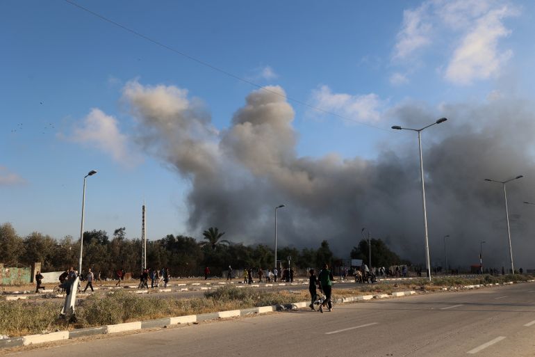 Smoke plumes rise during an Israeli strike as people walk along the Salah al-Din road near the Nusseirat refugee camp in the central Gaza Strip, used by food-seeking Palestinians to reach an aid distributution point set up by the privately-run Gaza Humanitarian Foundation (GHF), on June 25, 2025.